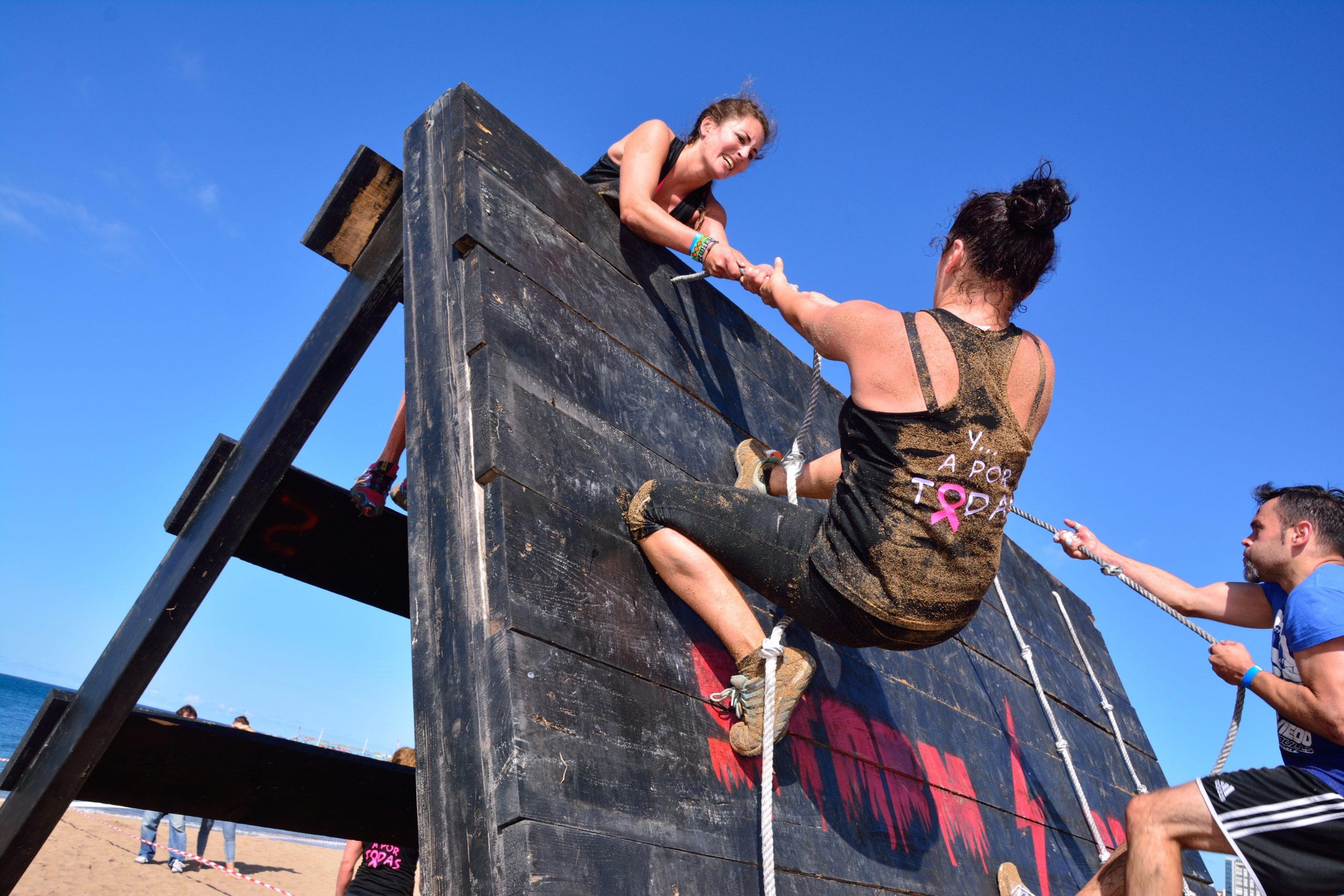 A woman climbing up a rope in a obstacle course with another woman offering to help