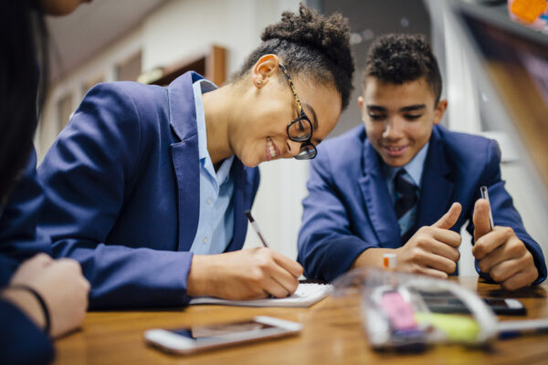 A school girl sitting at a desk writing on paper with a school boy sitting next to her